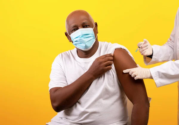 Médico que administra vacuna contra el coronavirus a un paciente varón afroamericano mayor con antecedentes de estudio naranja —  Fotos de Stock