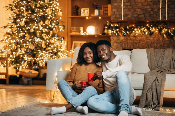 Alegre joven pareja negra celebrando la Navidad en casa, sentado en el suelo con café, pasar tiempo juntos en Navidad — Foto de Stock