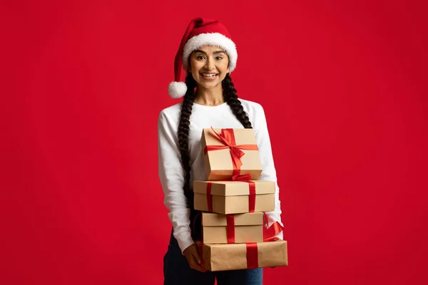 Vánoční dárky. Šťastná arabská dáma v Santa Klobouk držení stohu dárky — Stock fotografie