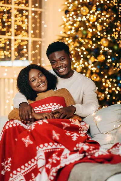 Sorrindo casal preto abraçando sob xadrez quente perto de abeto decorado na noite de Natal — Fotografia de Stock