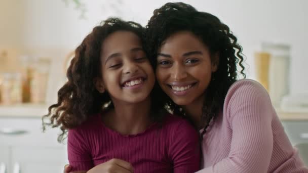 Glücklich liebende Familie. Fröhliche junge afrikanisch-amerikanische Mutter umarmt ihre kleine Tochter, lächelt gemeinsam in die Kamera — Stockvideo