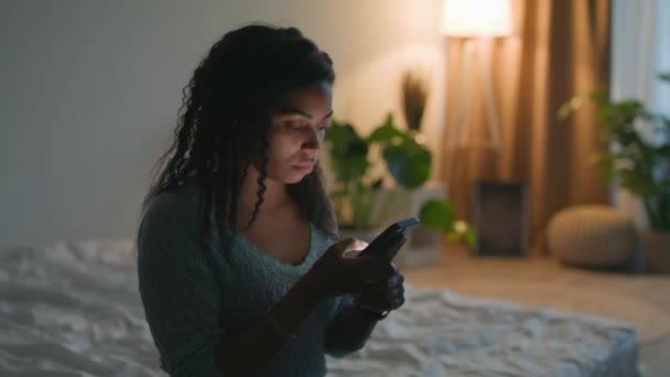 Adicción a los artilugios. Joven afroamericana americana web surf en el teléfono inteligente, sentado en habitación oscura en la noche en casa — Vídeo de stock