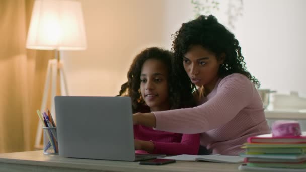 Älskar afrikansk amerikansk mor hjälpa sin dotter med läxor, förklara uppgift på laptop, hemma på kvällen — Stockvideo