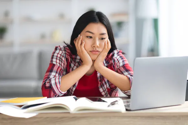 Проблемы онлайн-образования. Уставшая молодая азиатская студентка смотрит на экран компьютера — стоковое фото