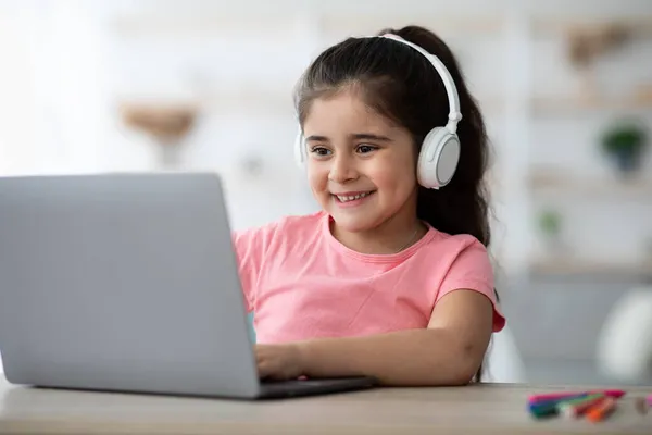 Bonito pouco árabe menina no sem fio fones de ouvido tendo on-line lição no laptop — Fotografia de Stock