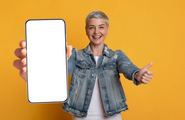 Pozitif orta yaşlı, kısa saçlı kadın akıllı telefon, model gösteriyor.