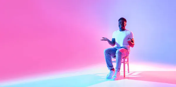 Volle Länge des glücklichen schwarzen Kerls, der auf einem Stuhl sitzt und freien Platz für Ihre Werbung in Neonlicht bietet, Banner — Stockfoto