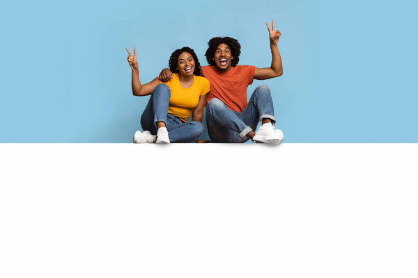 Carefree black couple sitting on blank board, gesturing