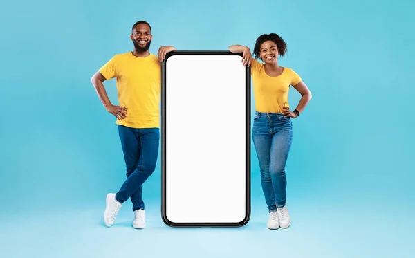 Casal afro-americano apoiando-se em smartphones gigantes com mockup, promovendo aplicativo ou site, anunciando seu serviço — Fotografia de Stock