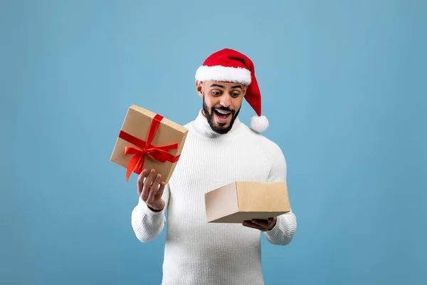 Hombre árabe alegre esperando la Navidad, abriendo la caja de regalo envuelta y mirando hacia el interior, posando sobre fondo azul — Foto de Stock