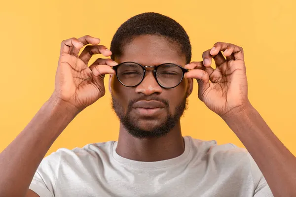 Afroamerikansk man med dålig syn bär glasögon och skelande ögon medan du tittar på kameran, gul bakgrund — Stockfoto