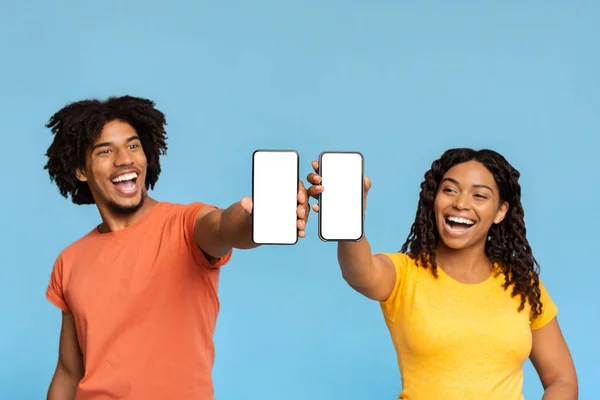 Wesoły czarny mężczyzna i kobieta pokazując smartfony z pustymi ekranami — Zdjęcie stockowe