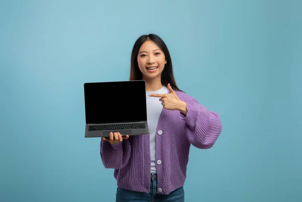 Online educational courses. Cheerful asian female student pointing at laptop with blank screen, blue studio background — Stock Photo, Image