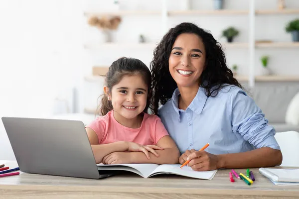 Mãe jovem fazendo lição de casa com a filha pequena, ajudando com o estudo em casa — Fotografia de Stock