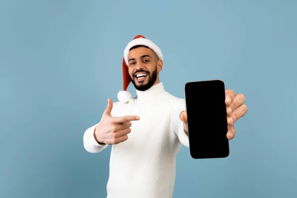 Hombre árabe feliz en sombrero de santa mostrando nuevo teléfono inteligente con pantalla en blanco, recomendando la aplicación móvil — Foto de Stock