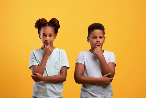 Pensivo menino preto e menina posando no fundo do estúdio amarelo — Fotografia de Stock