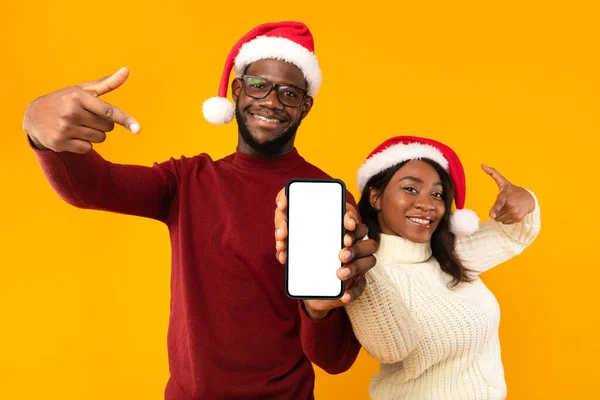African Couple Showing Smartphone Screen Wearing Santa Hats, Yellow Background — Stock Photo, Image