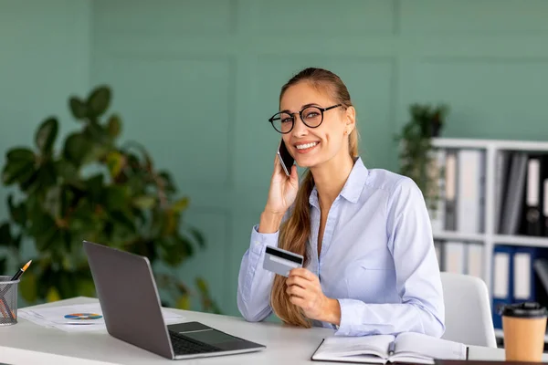 Freelancer feliz feminino encomendar on-line com cartão de crédito e smartphone, conversando com o gerente de atendimento ao cliente — Fotografia de Stock