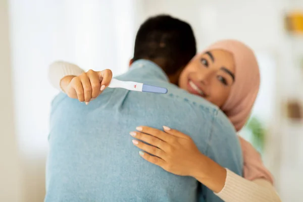 Emotionele moslim vrouw met positieve zwangerschapstest knuffelen haar man, glimlachen op de camera, close-up — Stockfoto