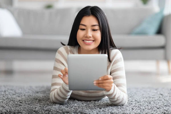 Tecnologie per il tempo libero. Bella asiatica femminile rilassante con tavoletta digitale a casa — Foto Stock