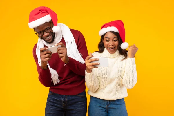 African Couple Playing Games On Smartphones Wearing Santa Hats, Studio — Stock Photo, Image