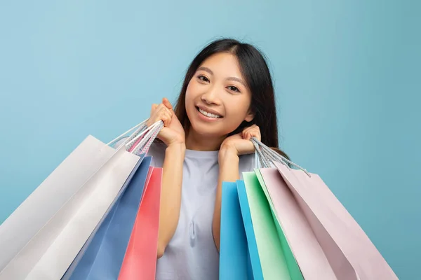 Svart fredagskoncept. Glad asiatisk dam efter framgångsrik shopping bär ljusa papperspåsar, blå bakgrund — Stockfoto