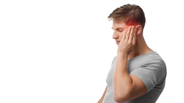 Unhappy young caucasian man suffering from headache, touches his forehead, highlighted in red — Stock Photo, Image