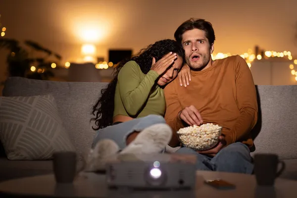 Shocked pareja viendo horror película cubriendo ojos usando proyector interior —  Fotos de Stock