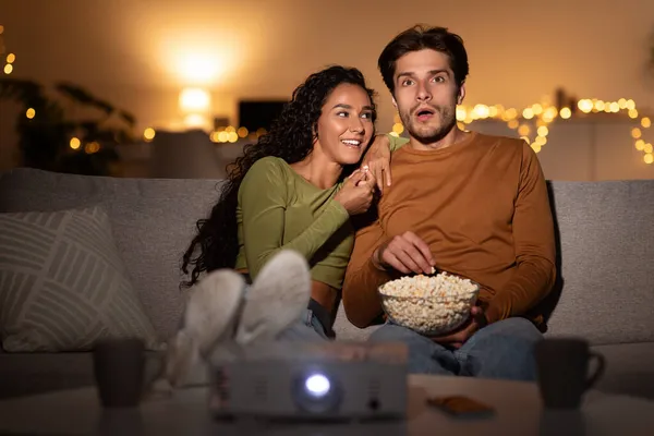 Spannend paar kijken film samen met behulp van projector het eten van popcorn Indoor — Stockfoto