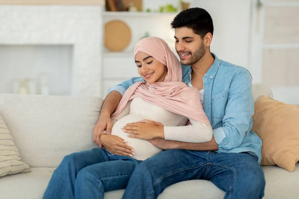 Amar esperando pareja árabe abrazos mientras pasar tiempo juntos en casa, sentado en el sofá, espacio libre — Foto de Stock