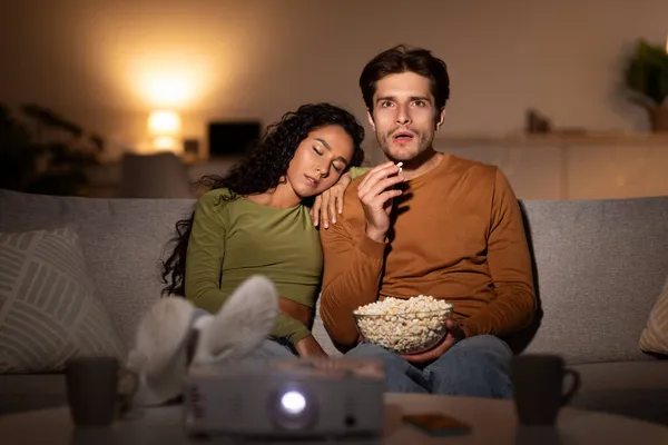 Ehefrau schlafen während ehemann beobachten film using projektor bei zuhause — Stockfoto