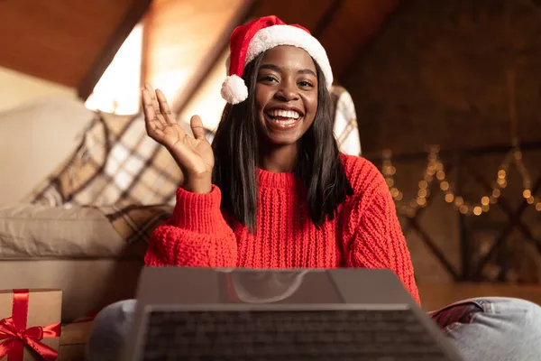 Positiv ung svart kvinna i Santa hatt och tröja vinka åt kameran, göra videosamtal, fira jul hemma — Stockfoto