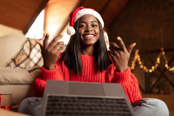 サンタ・ハットの若い黒人女性はノートパソコンを介して友人に話します,自宅からクリスマスや新年で家族を祝福 — ストック写真