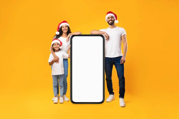 Arabische familie leunen op telefoon dragen Santa hoeden, Gele achtergrond — Stockfoto