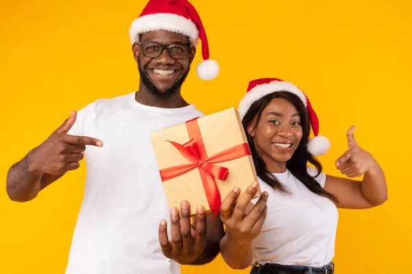 Afrikanska par håller julklapp Gesturing tummen upp över gul bakgrund — Stockfoto