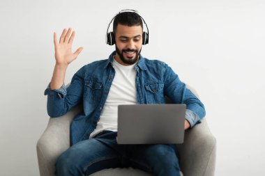 Genç bir Arap 'ın bilgisayarda internet görüşmesi ya da video konferansı olması, kulaklık takması, kameraya konuşması, koltukta oturması.