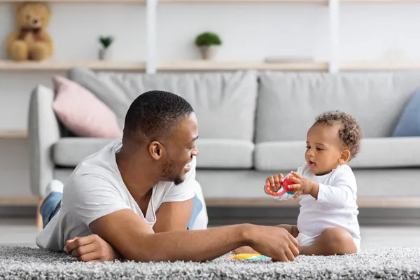 Licença Parental Partilhada. Jovem pai negro brincando com pouco bebê em casa — Fotografia de Stock
