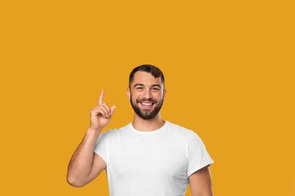 Feliz hombre caucásico de mediana edad en camiseta blanca apuntando hacia arriba en el dedo en el espacio vacío —  Fotos de Stock