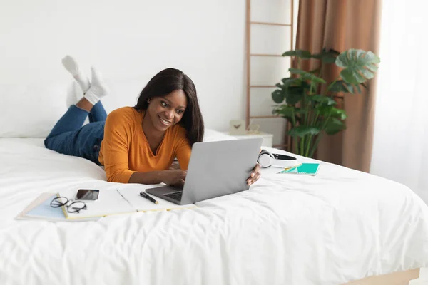 Feliz señora freelancer negro usando el ordenador portátil de trabajo en línea en el dormitorio — Foto de Stock