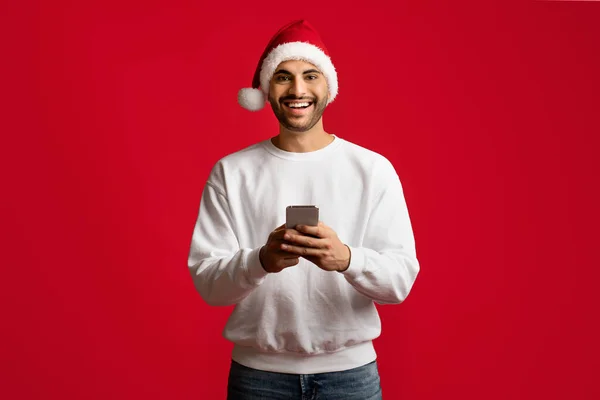移动应用程序。快乐的阿拉伯男人手握智能手机，头戴圣诞帽 — 图库照片