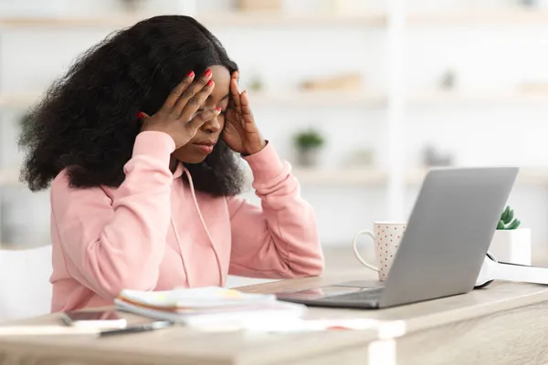 Mujer negra estresada sentada frente al portátil, tocando la cabeza — Foto de Stock