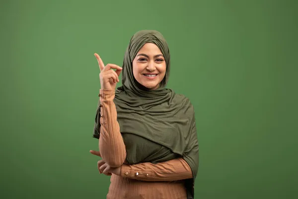 Wanita islamik positif dalam hijab memiliki ide, menunjuk ke atas, memiliki momen inspirasional di atas latar belakang zaitun — Stok Foto
