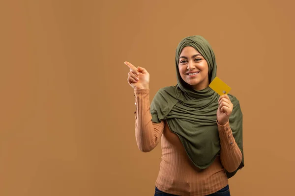 興奮arab女性でhihab保持クレジットカード指摘脇にフリースペース上のブラウンスタジオ背景 — ストック写真