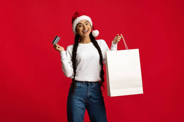 Noel alışverişi. Elinde boş kağıt çanta ve kredi kartı tutan neşeli bir Arap kadını. — Stok fotoğraf