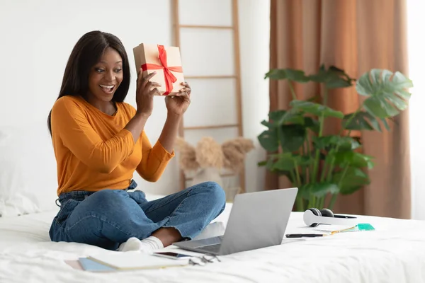 Emocionada dama africana celebración de videollamadas de regalo a través de ordenador portátil de interior —  Fotos de Stock
