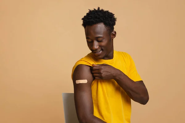 Vacunado de Covid-19. Joven hombre negro mirando vendaje adhesivo en brazo —  Fotos de Stock
