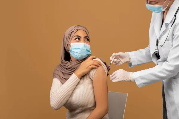 Vacunación Covid-19. Médico que da inyección de vacunación, vacunando a la señora musulmana sobre fondo marrón — Foto de Stock
