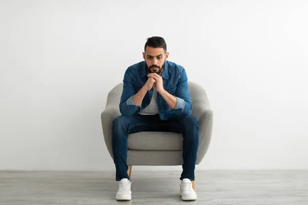 Arap adam kasvetli bir ifadeyle koltukta oturuyor, üzgün ya da yorgun hissediyor, sorun yaşıyor, depresyon geçiriyor. — Stok fotoğraf
