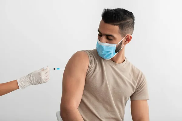 Hombre árabe joven con mascarilla facial que recibe la vacunación contra el coronavirus, recibiendo la inmunización covid-19 —  Fotos de Stock