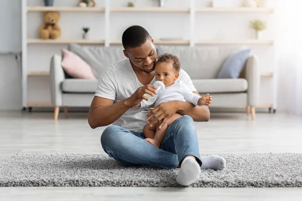 Concepto de cuidado de niños. Amar al padre afroamericano dando biberón con agua al bebé — Foto de Stock